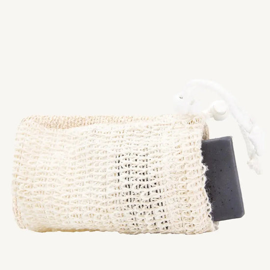 A beige natural sisal soap saver bag with a dark grey soap bar inserted, tied with a white string.