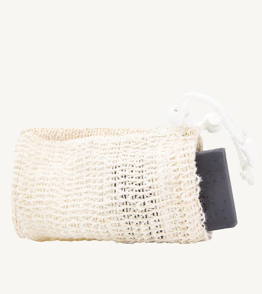 A beige natural sisal soap saver bag with a dark grey soap bar inserted, tied with a white string.