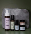 A Starter Skincare Kit for acne-prone skin with a foaming face wash, Clean Sweep Toner, Nightly Face Serum, Beauty Balm, Face Cream, and a gray cosmetic bag on a green background.