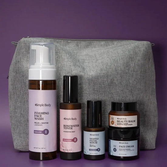 A Starter Skincare Kit for mature skin with a foaming face wash, Rosewater Toner, Nightly Face Serum, Beauty Balm, Face Cream, and a gray cosmetic bag on a purple background.