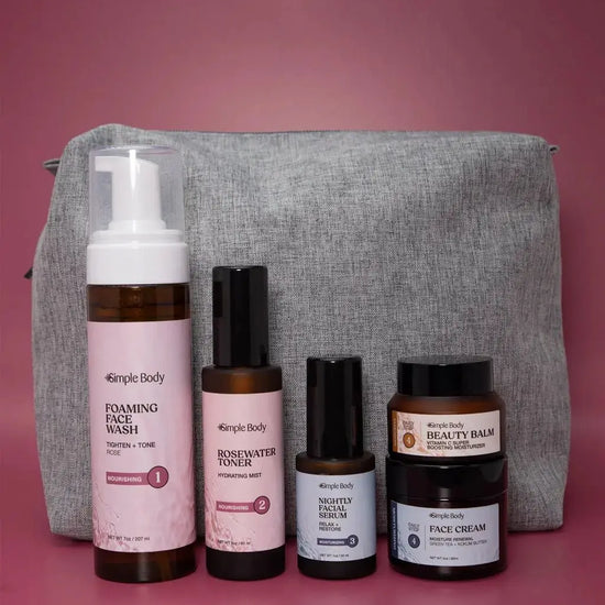 A Starter Skincare Kit for Normal to Dry skin with a foaming face wash, Rosewater Toner, Nightly Face Serum, Beauty Balm, Face Cream, and a gray cosmetic bag on a rosy pink background.