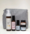 A Starter Skincare Kit for Sensitive Skin with a foaming face wash, Rosewater Toner, Nightly Face Serum, Beauty Balm, Face Cream, and a gray cosmetic bag on a yellow background.