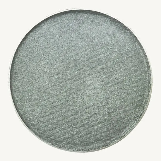 A photo of Pure Anada's Pressed Eye Color in Sterling which is a bluish green shimmery color on a tan background.