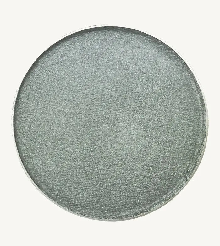 A photo of Pure Anada's Pressed Eye Color in Sterling which is a bluish green shimmery color on a tan background.