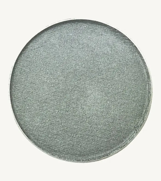 A photo of Pure Anada's Pressed Eye Color in Sterling which is a bluish green shimmery color on a tan background.