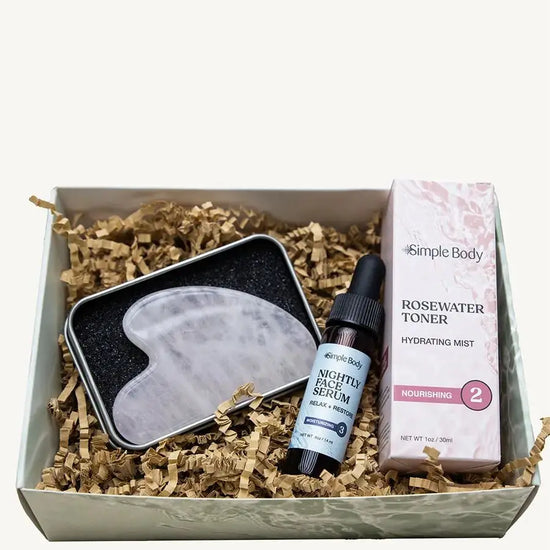 Simple Body Gua Sha gift set including a gua sha tool, Nightly Face Serum, and a Rosewater Toner in a box with crinkled paper