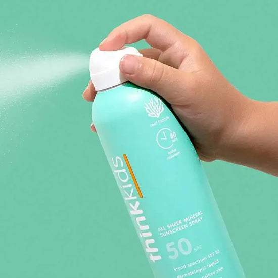 Hand holding a blue sunscreen spray bottle with a green background