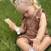 Child sitting on grass holding a tube of Think Baby Sensitive sunscreen