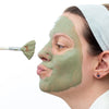 Person applying a Simple Body French Green Clay mask to their face with a brush on a white background