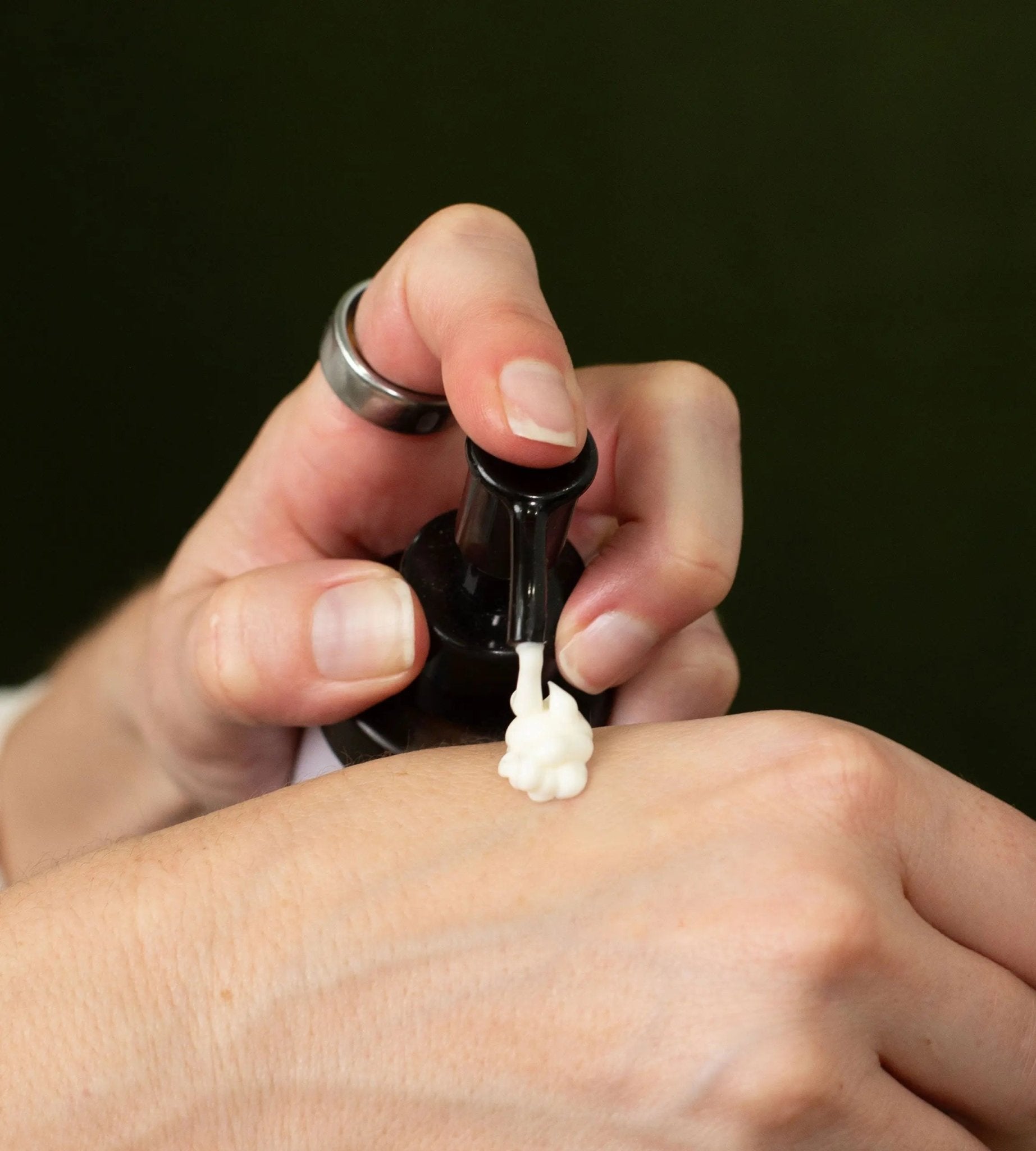 A hand holding a bottle of Simple Body Lotion pumping it onto a hand showing the creamy off white texture.