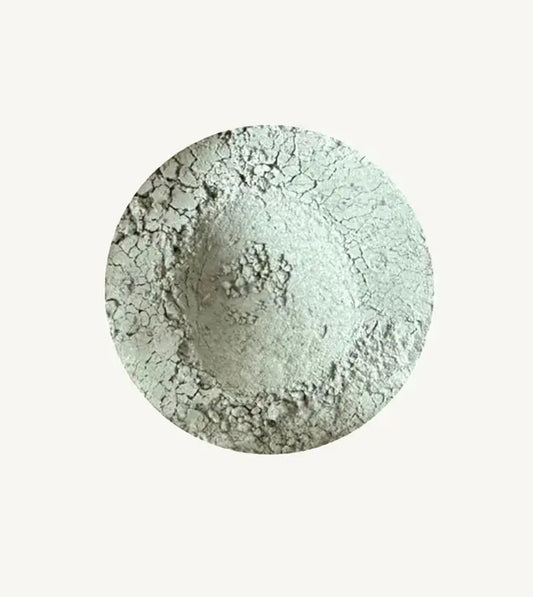 A photo of Pure Anada's Velvet Loose Matte Eyeshadow in Gray Flannel which is a light gray green color on a tan background.