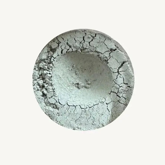 A photo of Pure Anada's Velvet Matte Loose Eyeshadow in Chambray which is a light silvery-gray with a hint of green on a tan background.