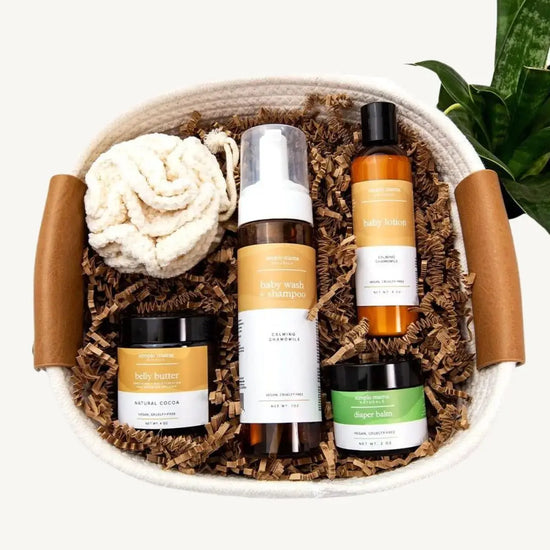A Welcome Baby Gift Basket containing a Baby Wash, Baby Lotion, Belly Butter, and Diaper Balm, plus a cotton pouf, all beautifully arranged in a natural rope basket.