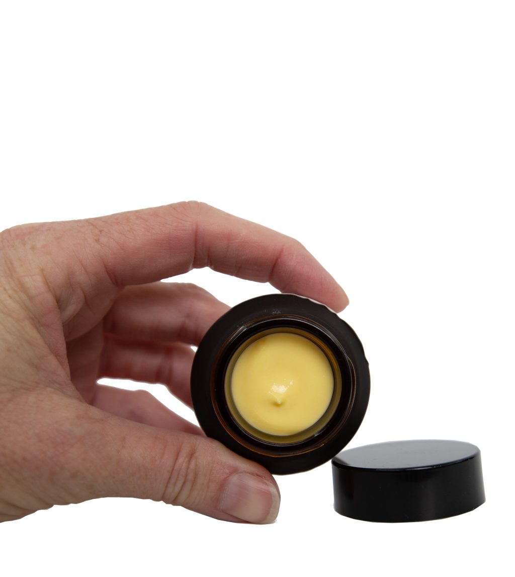 Hand holding a mini beauty balm with the lid off and a yellow, creamy moisturizer showing